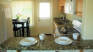 A kitchen with granite countertops, a stove, and a dining area with a table and chairs.