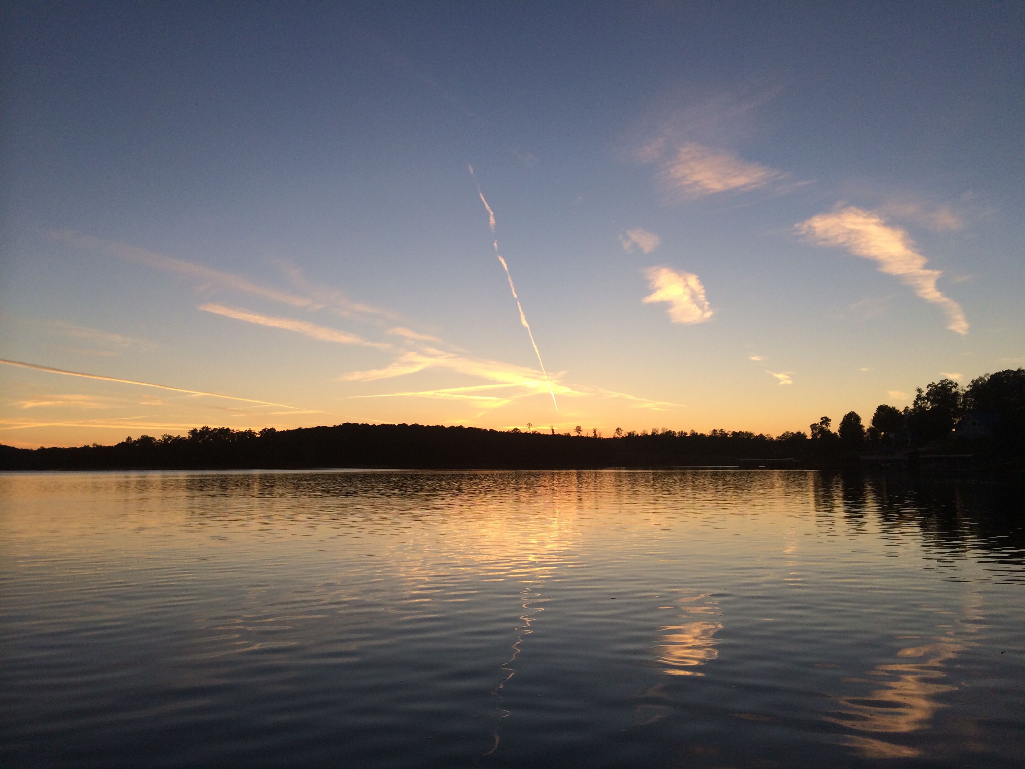 A calm lake at sunset with a clear sky and distant trees.