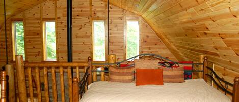 Ein Schlafzimmer einer Holzhütte mit einem Bett, einem Holz-Kopfteil und einem Fenster.