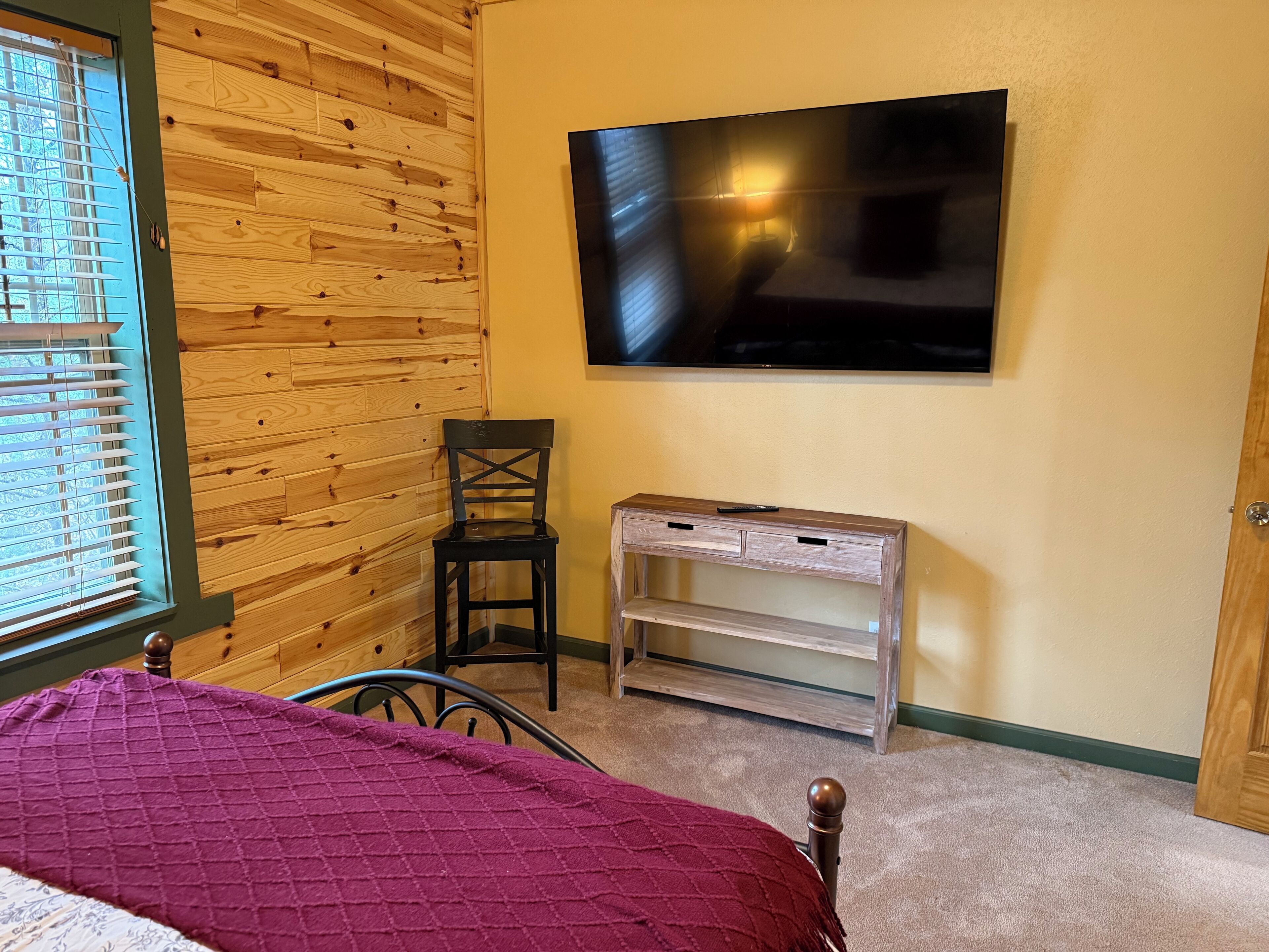 A bedroom with a bed, a wooden wall, a TV, and a desk.