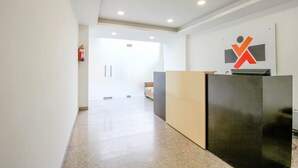 Un área de recepción con diseño moderno, que incluye un mostrador de recepción, un extintor y una puerta que da a otra habitación.