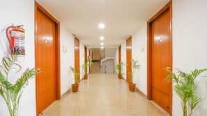 Un pasillo con puertas de madera, plantas en macetas y un extintor en la pared.