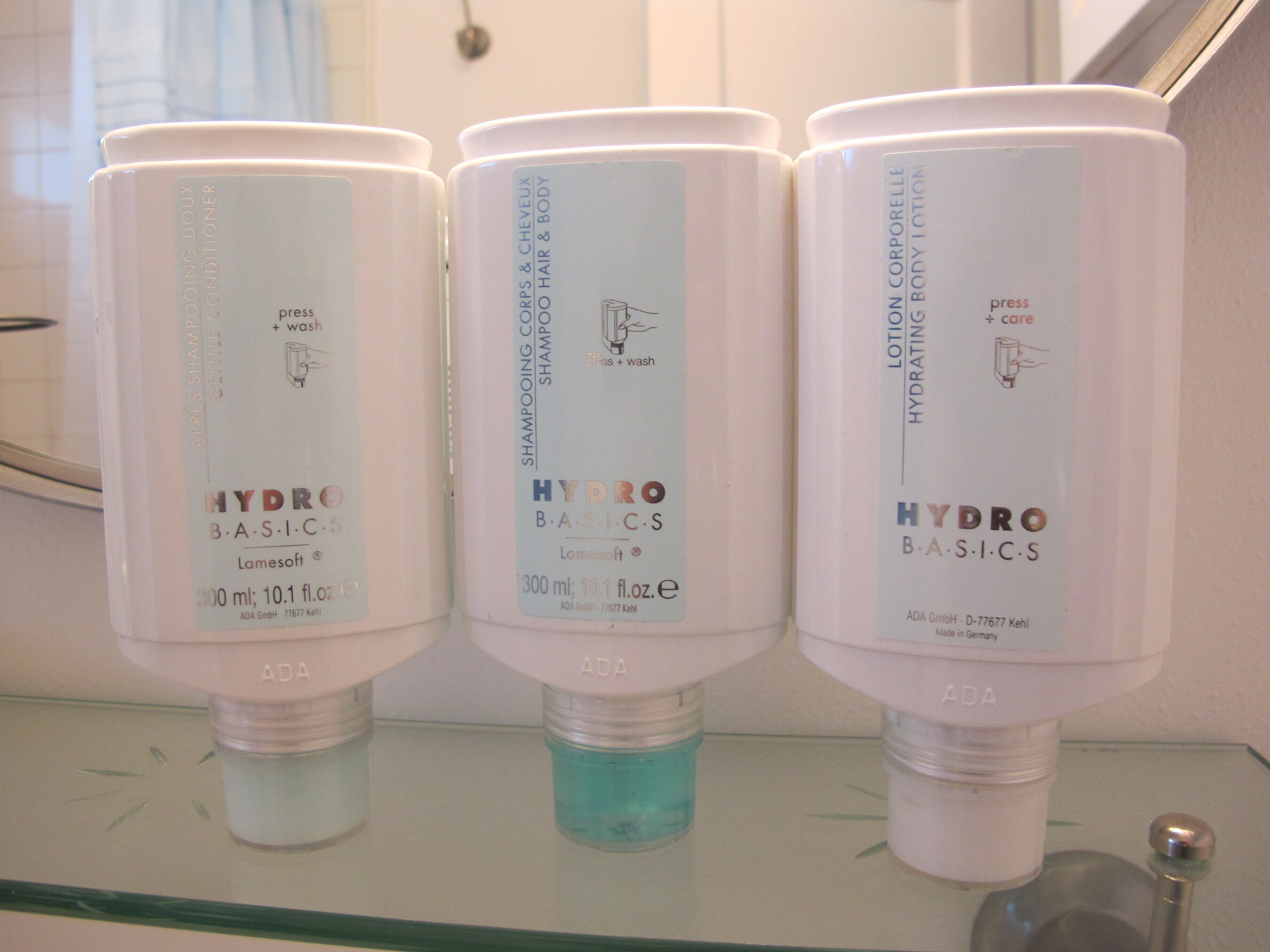 Three bottles of Hydra Basics shampoo and conditioner on a bathroom shelf.