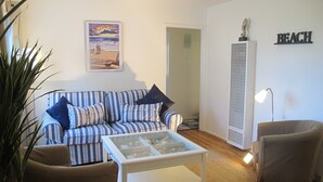 A living room with a striped sofa, a glass-top coffee table, a brown armchair, a lamp, and a wall-mounted sculpture. - Chic Beach Apartment..Steps to the sand! (San Diego)