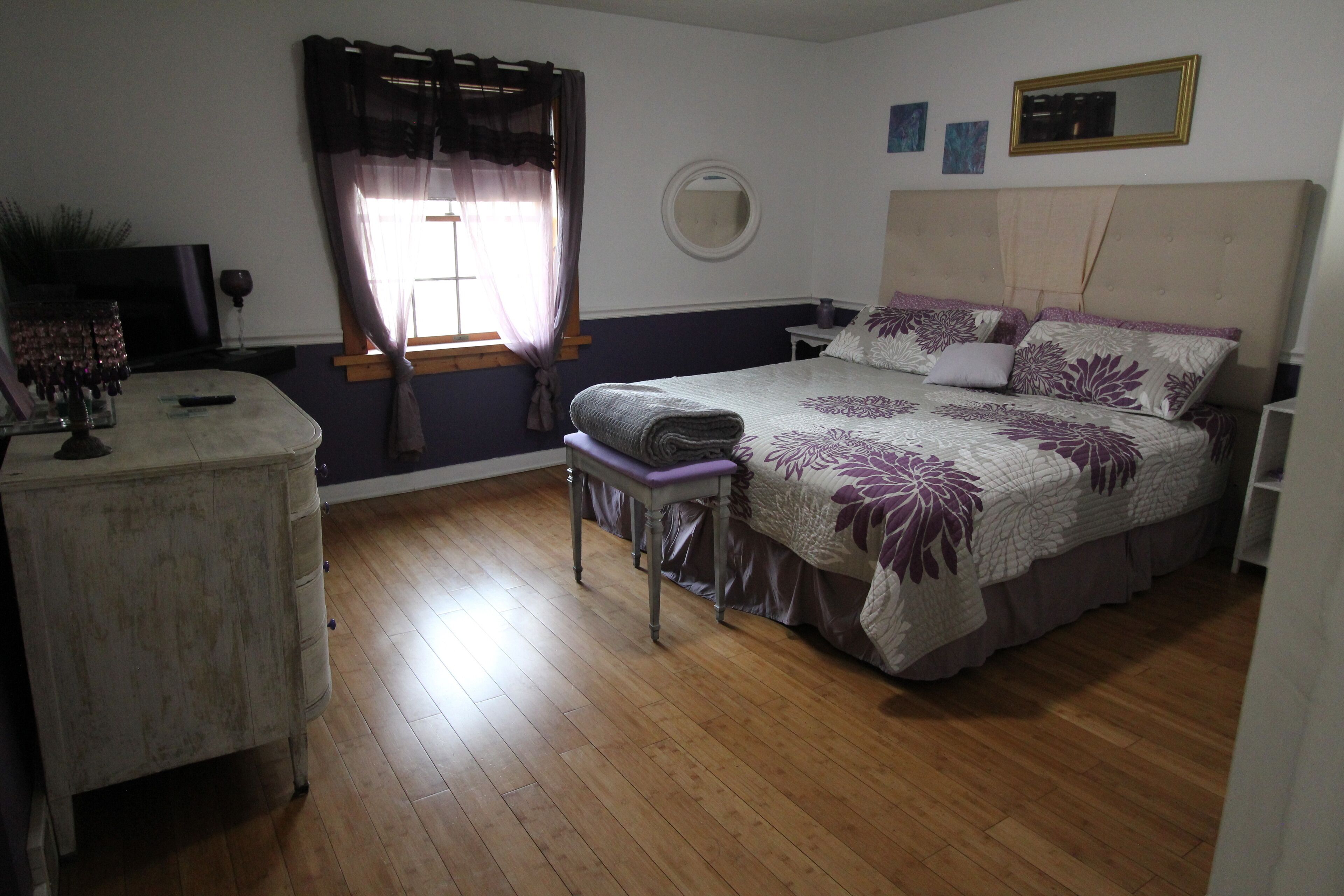 A bedroom with a bed, a bedside table, a chair, a dresser, a mirror, and a window with curtains.