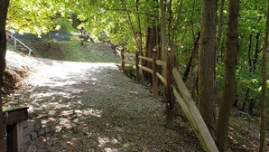 Un sendero de grava que serpentea por un área boscosa con una valla de madera y un farol de metal.