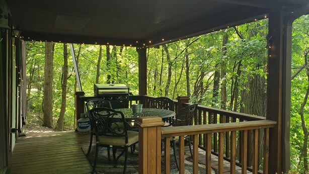 Terraza techada al aire libre con una mesa y sillas, rodeada de un bosque.