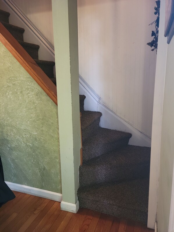 A staircase with carpeted steps leading to a landing, a wooden handrail, and a green wall.