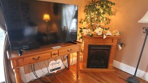 Una sala de estar con televisor de pantalla plana, mueble de madera para entretenimiento, chimenea y una planta en maceta.