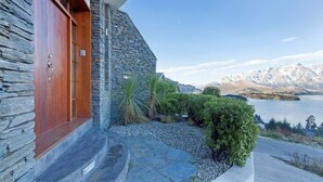 A stone building with a wooden door, a stone staircase, and a view of a lake and mountains. - BELVEDERE-(meaning in Italian PANORAMIC VIEWS) 3 BEDROOM HOUSE IN QUEENSTOWN (Fernhill)