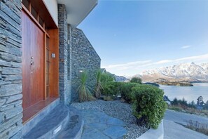 Steps lead up to the entrance of this building, situated near a body of water with mountains in the background.