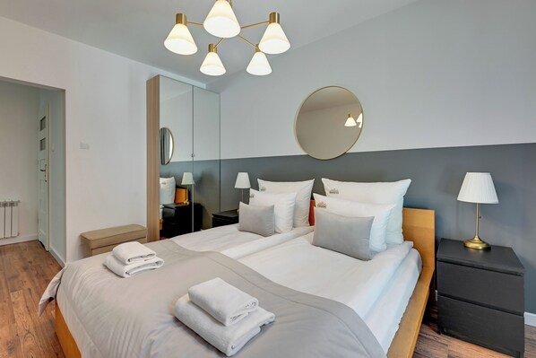Une chambre d’hôtel moderne avec un grand lit, des tables de chevet, un miroir et un luminaire au plafond.