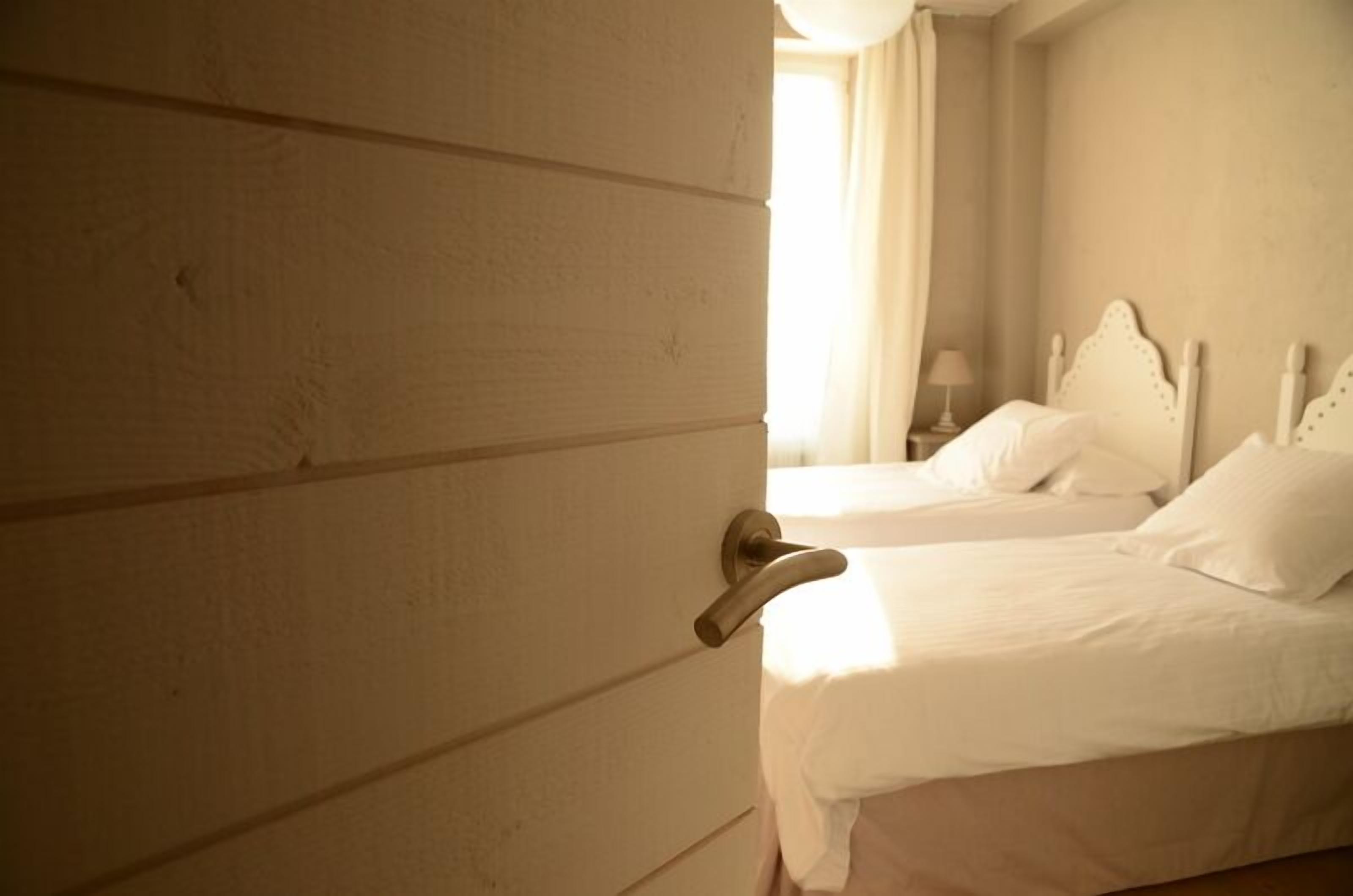 Ein Hotelzimmer mit zwei Betten, einer Holztür und einem Fenster mit Vorhängen.