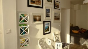 Una sala de estar con una butaca blanca, un sofá gris y una pared decorada con marcos y estanterías.