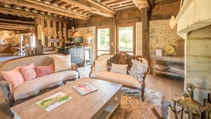 Un intérieur rustique avec des poutres apparentes, une cheminée en pierre et un coin salon confortable agrémenté d’une table basse.
