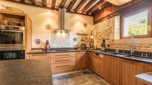 Une cuisine avec des meubles en bois, une hotte de cuisinière en acier inoxydable, un pare-feu en pierre et une fenêtre donnant sur un paysage verdoyant.