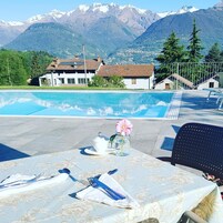 Área de refeições à beira da piscina, com mesa posta para dois, com vista para uma paisagem montanhosa.