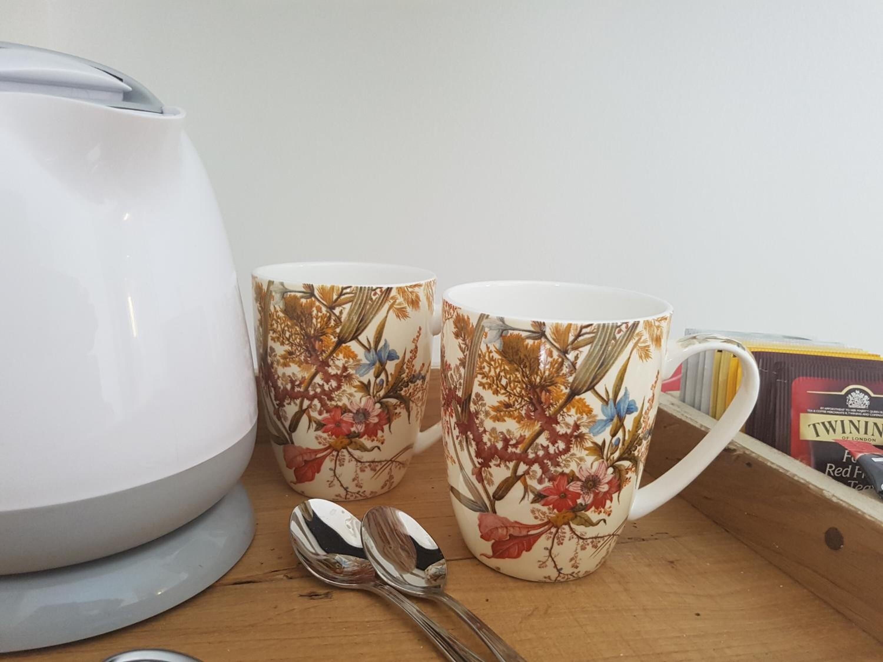 Dos tazas estampadas con flores sobre una superficie de madera, junto a una tetera blanca y una caja de té Twinings.