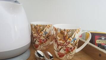 Dos tazas estampadas con flores sobre una superficie de madera, junto a una tetera blanca y una caja de té Twinings.