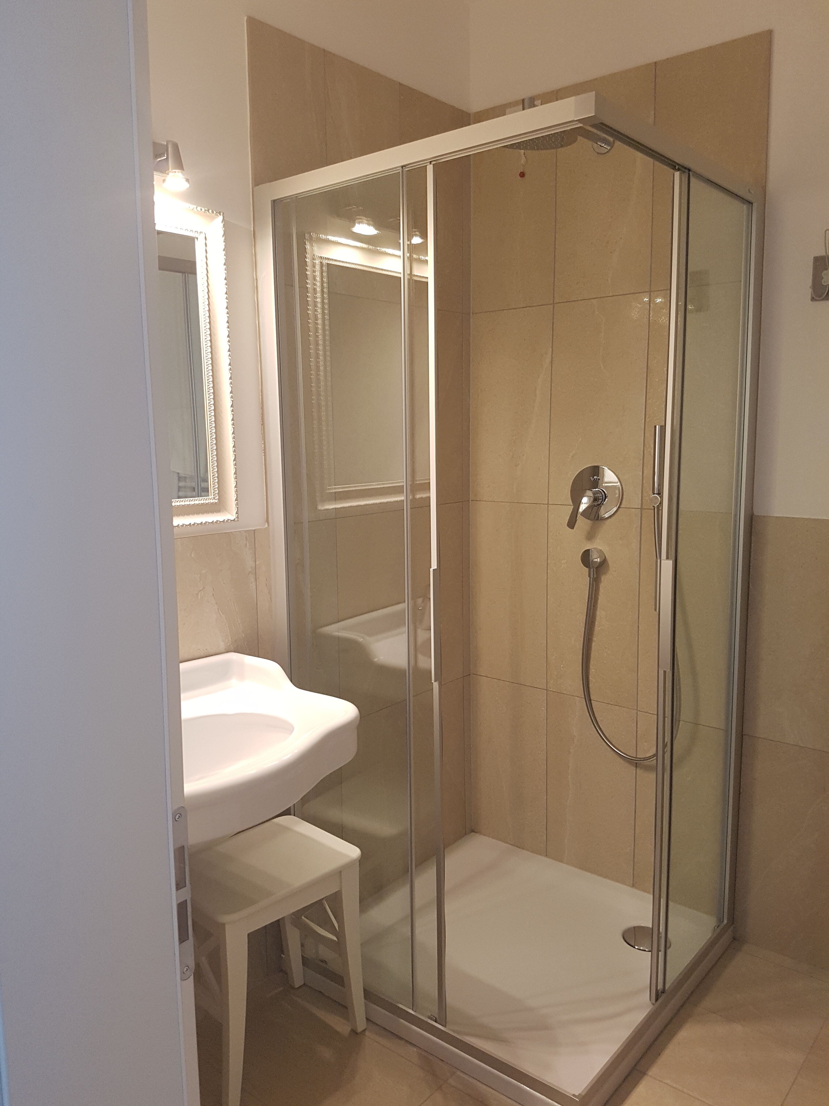 Un baño moderno con ducha envuelta en vidrio, un lavabo blanco y un espejo encima.