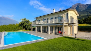 A two-story house with a swimming pool, a covered patio, and a mountain backdrop.