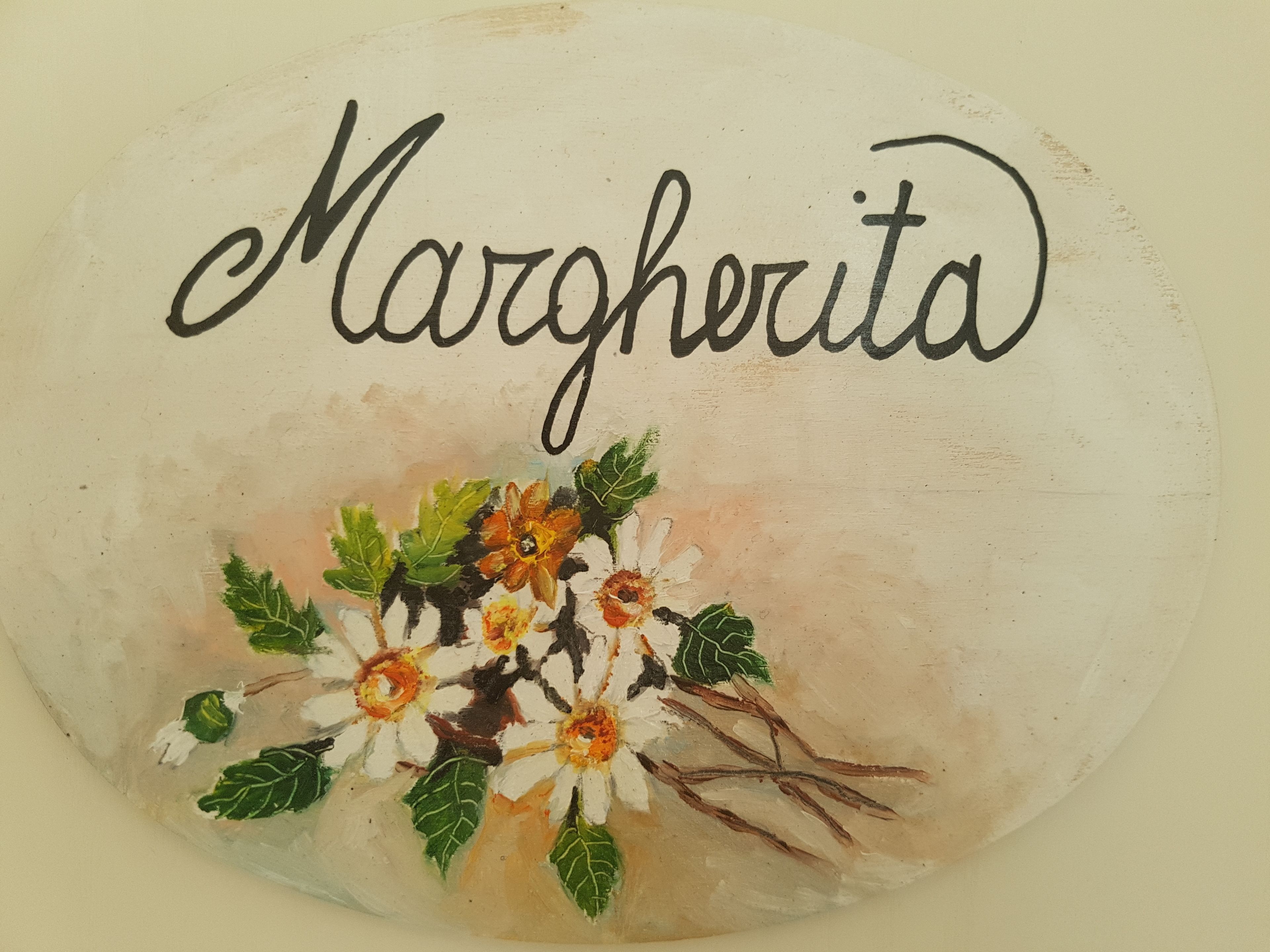 Una piedra pintada con el texto "Margherita" y un arreglo floral.