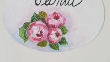 Un panneau circulaire portant le nom « Peonia » et une aquarelle représentant trois fleurs roses aux feuilles vertes.