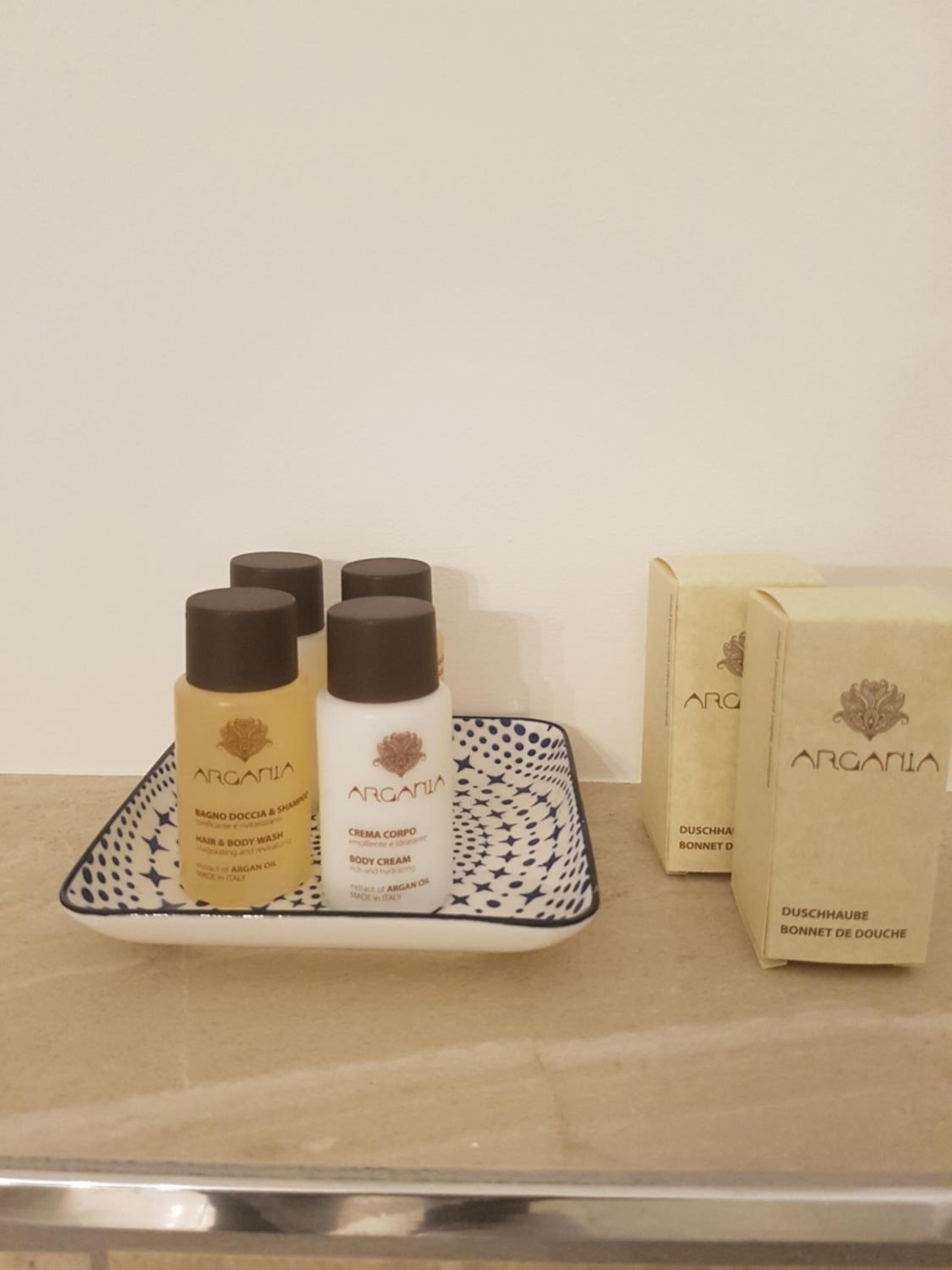 Ein Tablett mit zwei Flaschen Argania Körpercreme und zwei Packungen Argania Haar- und Duschgel auf einer gefliesten Oberfläche.