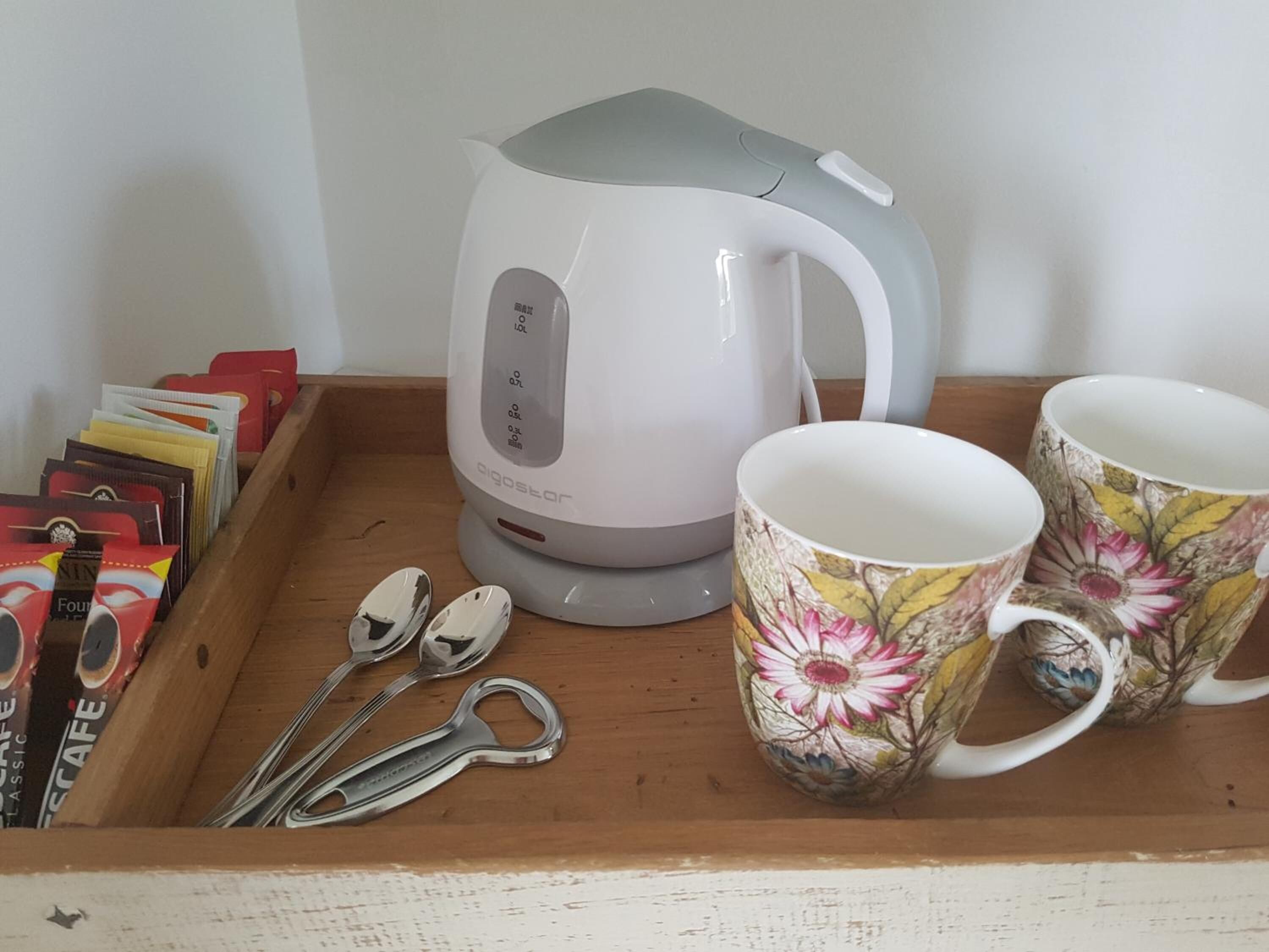 Una bandeja con una tetera blanca, dos tazas con motivos florales y un juego de cucharas de plata.