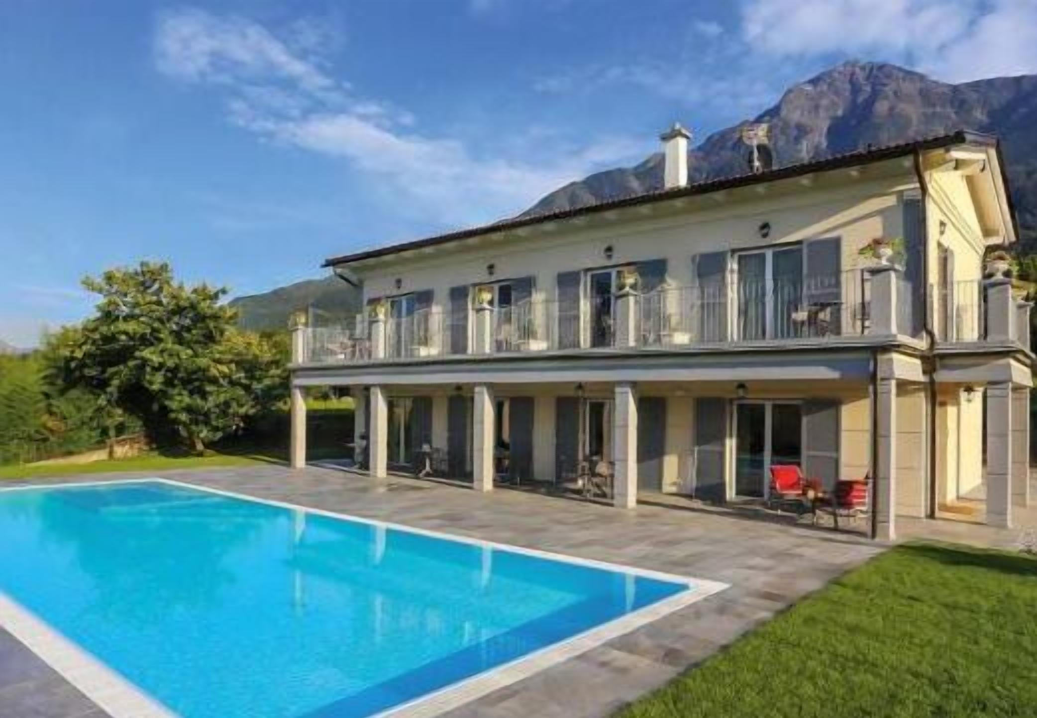 Ein zweistöckiges Haus mit Schwimmbecken im Vordergrund und Bergen im Hintergrund.