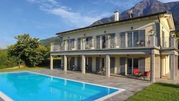 Ein zweistöckiges Haus mit Schwimmbecken im Vordergrund und Bergen im Hintergrund.