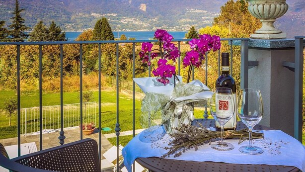 A balcony with a table set for two, featuring a bottle of wine, glasses, and a vase with flowers.
