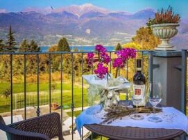 Varanda com mesa posta para dois, com uma garrafa de vinho, copos e um vaso de flores.