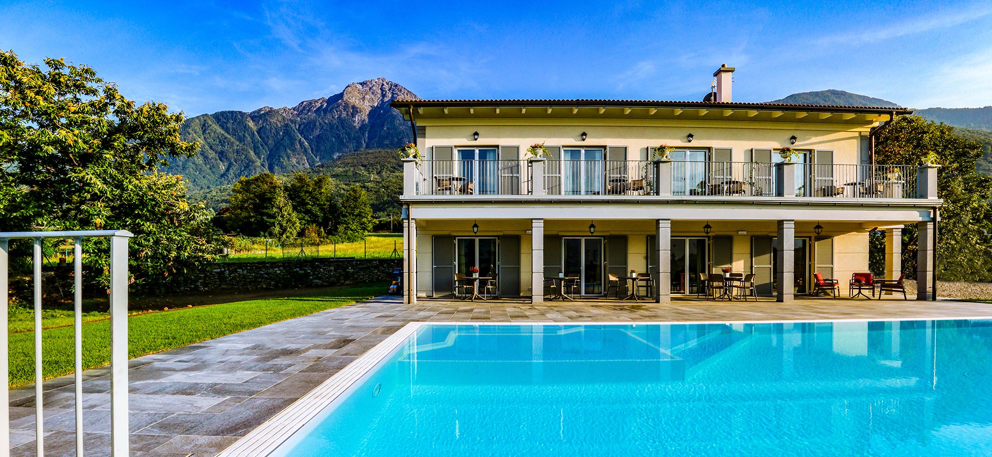 A two-story house with a swimming pool, outdoor seating, and a mountainous backdrop.