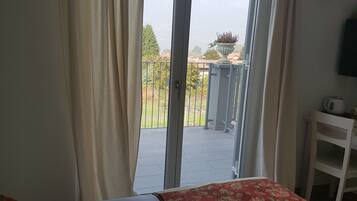 Un dormitorio con cama, una mesita y vistas a un jardín a través de un ventanal corredera.