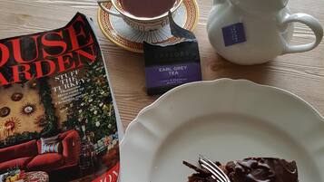 A table with a book titled 'House Garden', a teapot, a cup of tea, and a slice of chocolate cake on a plate.