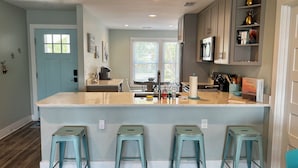 A modern kitchen with a central island, bar stools, a microwave, and a coffee maker. - Sea Salt Cottage - Beach front neighborhood, next to downtown restaurants (Isle of Palms)
