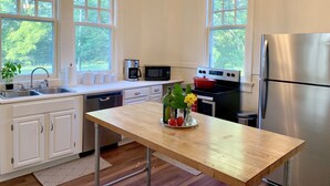A modern kitchen with white cabinets, a wooden countertop, a stainless steel refrigerator, and large windows offering a view of greenery. - Beautiful Farmhouse near Tuscaloosa (Fayette)