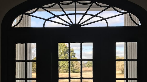 A dark interior view of a room with a large arched window overlooking a grassy area. - Beautiful Farmhouse near Tuscaloosa (Fayette)