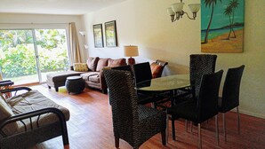 Una sala de estar con sofá, mesa de comedor, sillas y un cuadro de una playa.