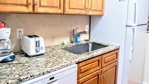Una cocina con armarios de madera, encimera de granito, lavavajillas blanco, tostadora, pileta con grifo y refrigerador blanco.