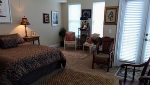 A bedroom with a large bed, a chair, a lamp, and a door with blinds. - Stylish Townhome by K&P Hotel - LABOR DAY SPECIAL, 5 for 4; 4 for 3.5 (St. Simons Island)