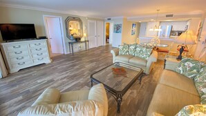 Ein geräumiges Wohnzimmer mit einem großen Sofa, einem Glastisch und einem Fernseher auf einer weißen Kommode.