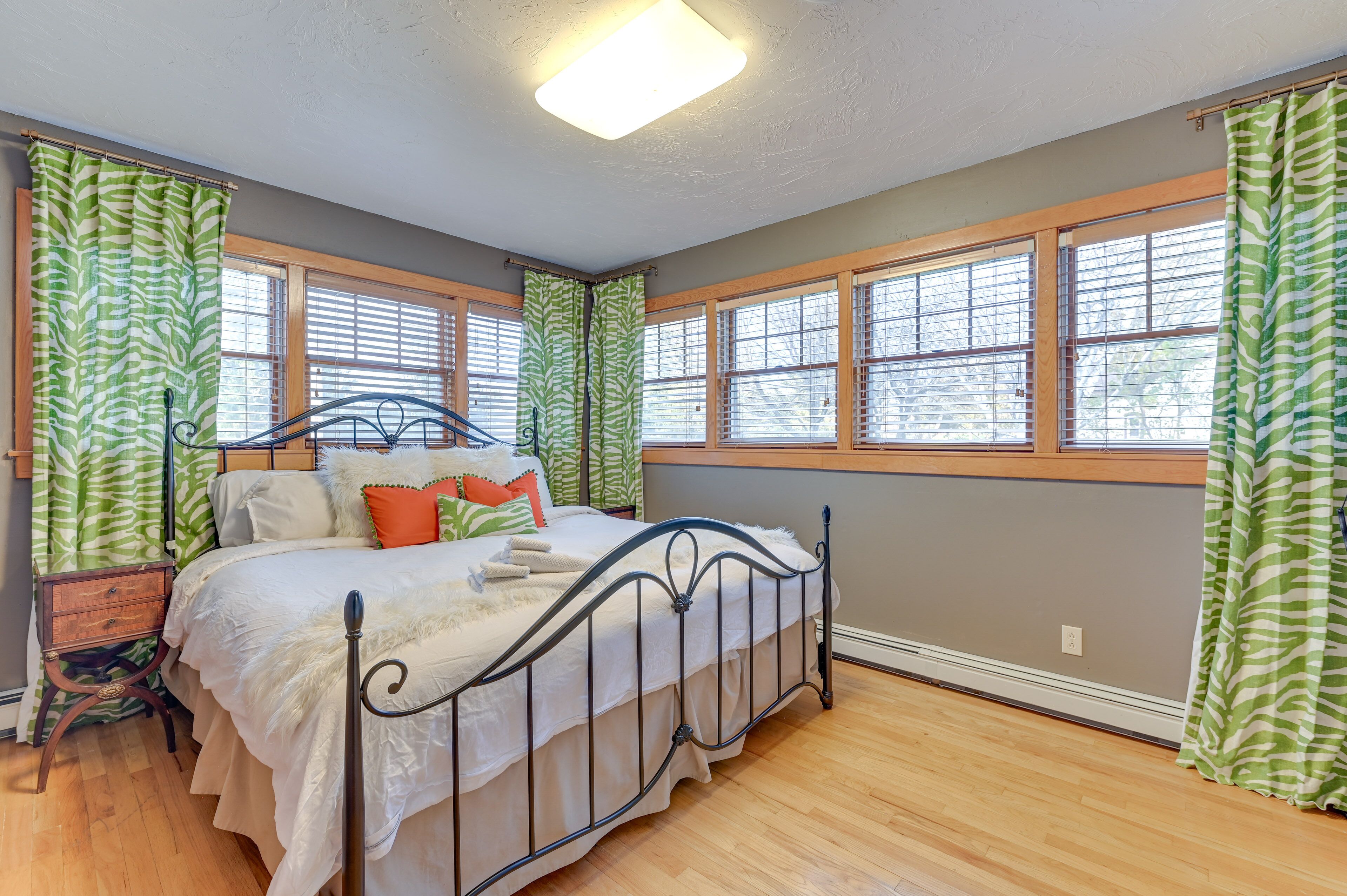 A bedroom with a bed, wooden floor, and large windows with green curtains.