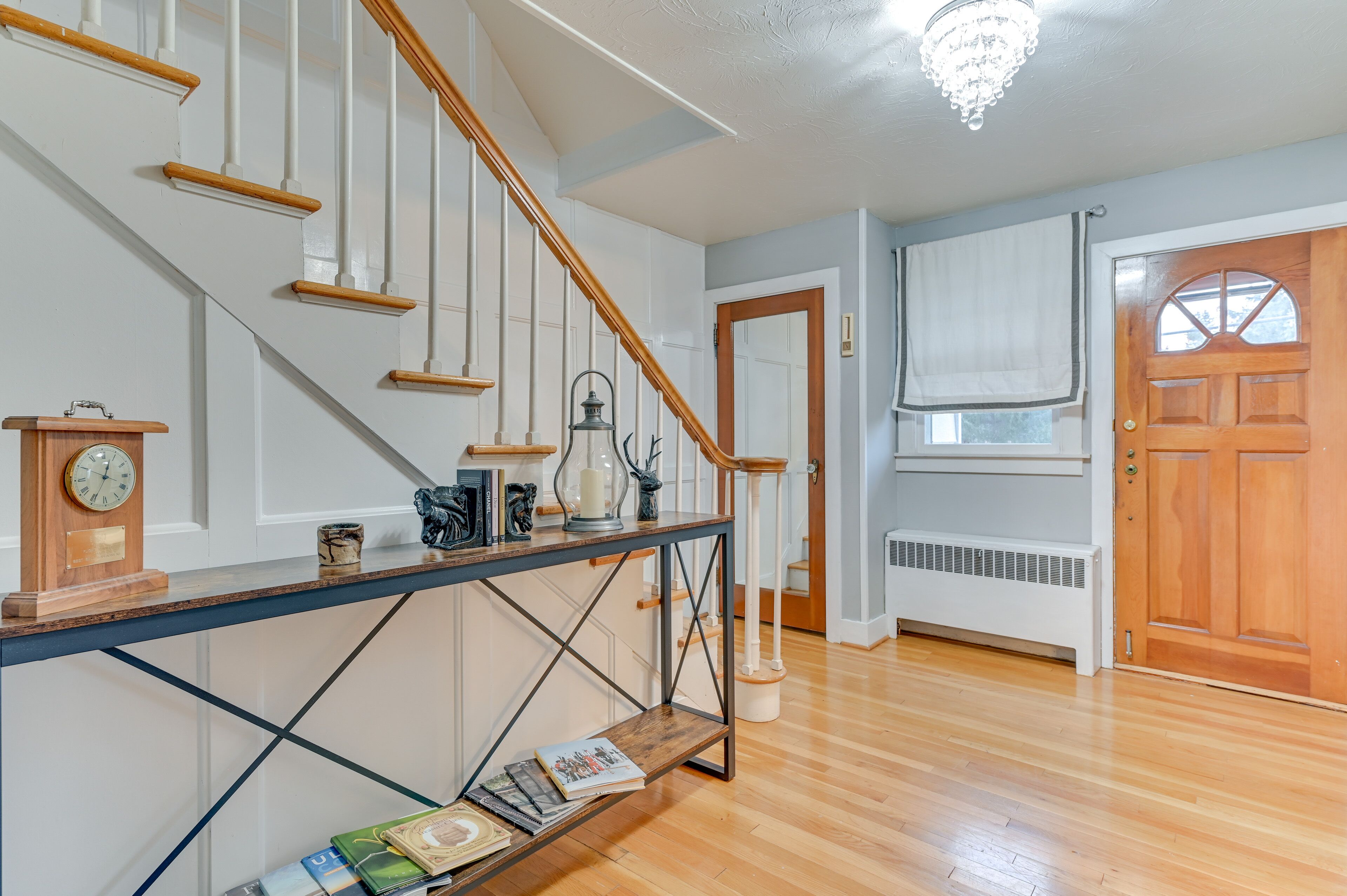 A staircase with wooden handrails, a console table with a clock, a floor lamp, and a radiator near a door.