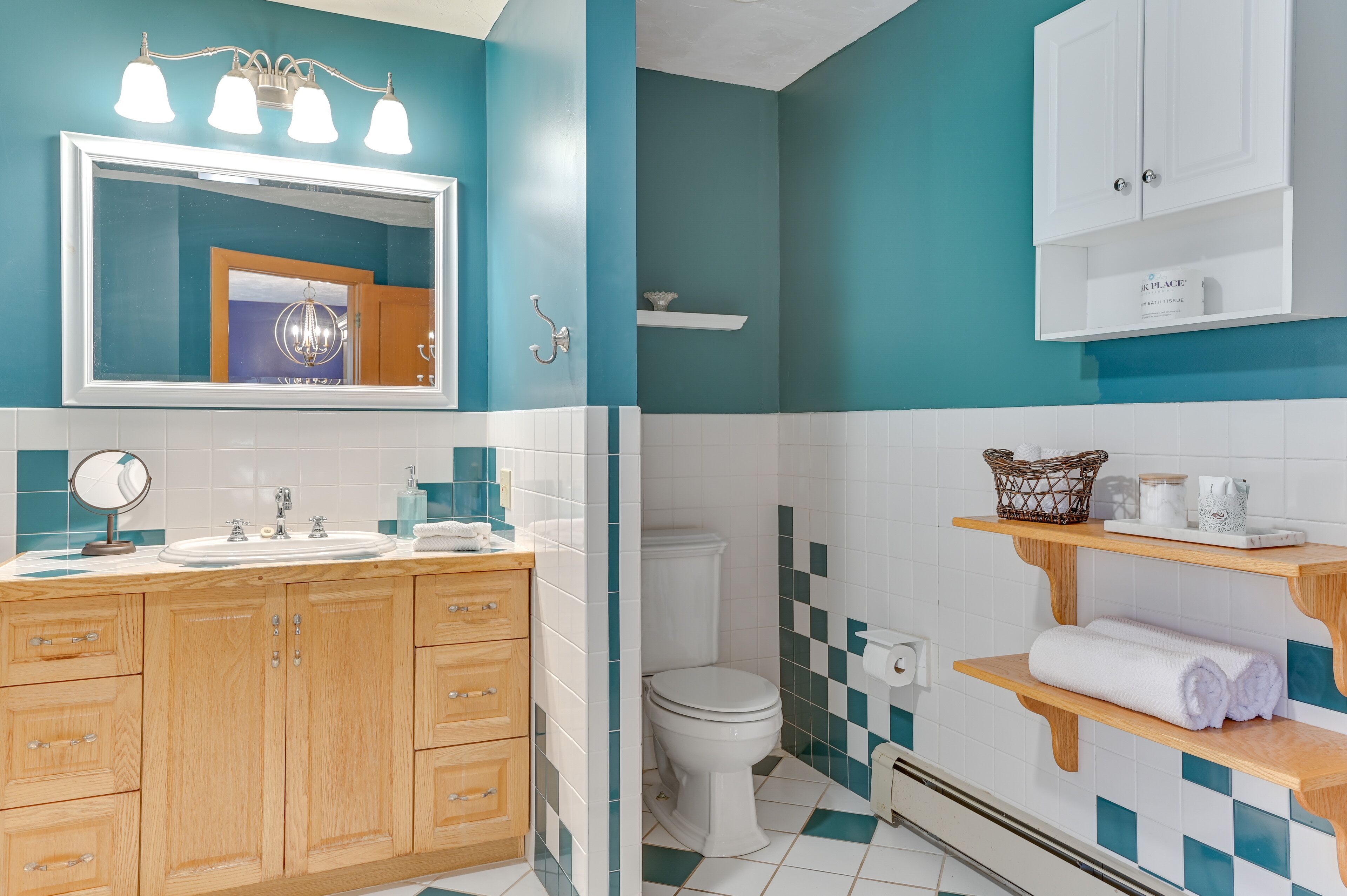 A bathroom with a wooden vanity, a large mirror, a sink, and a toilet. There are shelves with towels and toiletries.