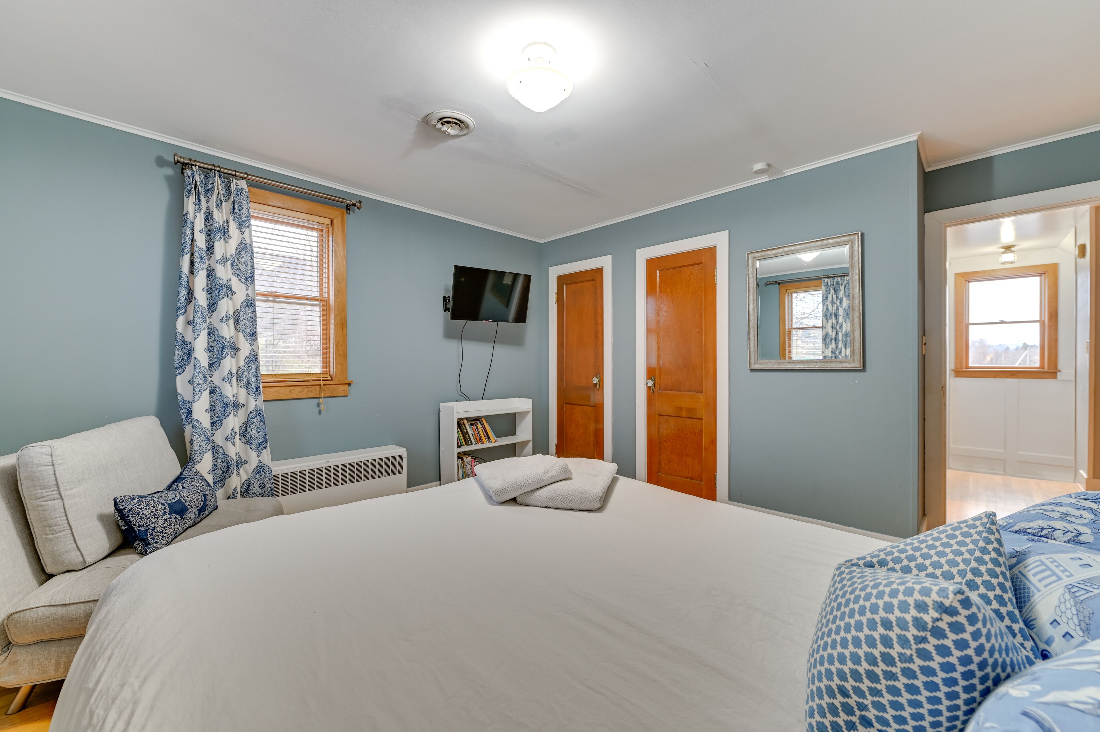 Un dormitorio con una cama grande, un televisor montado en la pared y una ventana con persianas.