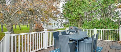 A deck with a table and chairs, surrounded by a white fence, with trees and a house in the background.