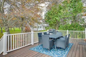 Une terrasse avec une table et des chaises, entourée d’une clôture blanche, avec des arbres et une maison en arrière-plan.
