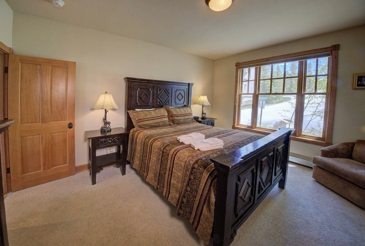 Une chambre avec un grand lit, deux tables de chevet avec des lampes, une porte en bois, une fenêtre avec vue et un canapé marron.